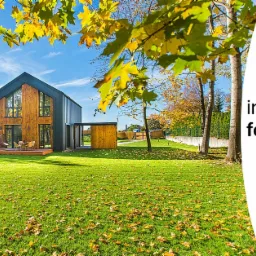 Dwa panele fotowoltaiczne na tle nowoczesnych domów z drewnianą elewacją i zielonym trawnikiem pokrytym jesiennymi liśćmi, widoczny fragment logo Partner GSE.