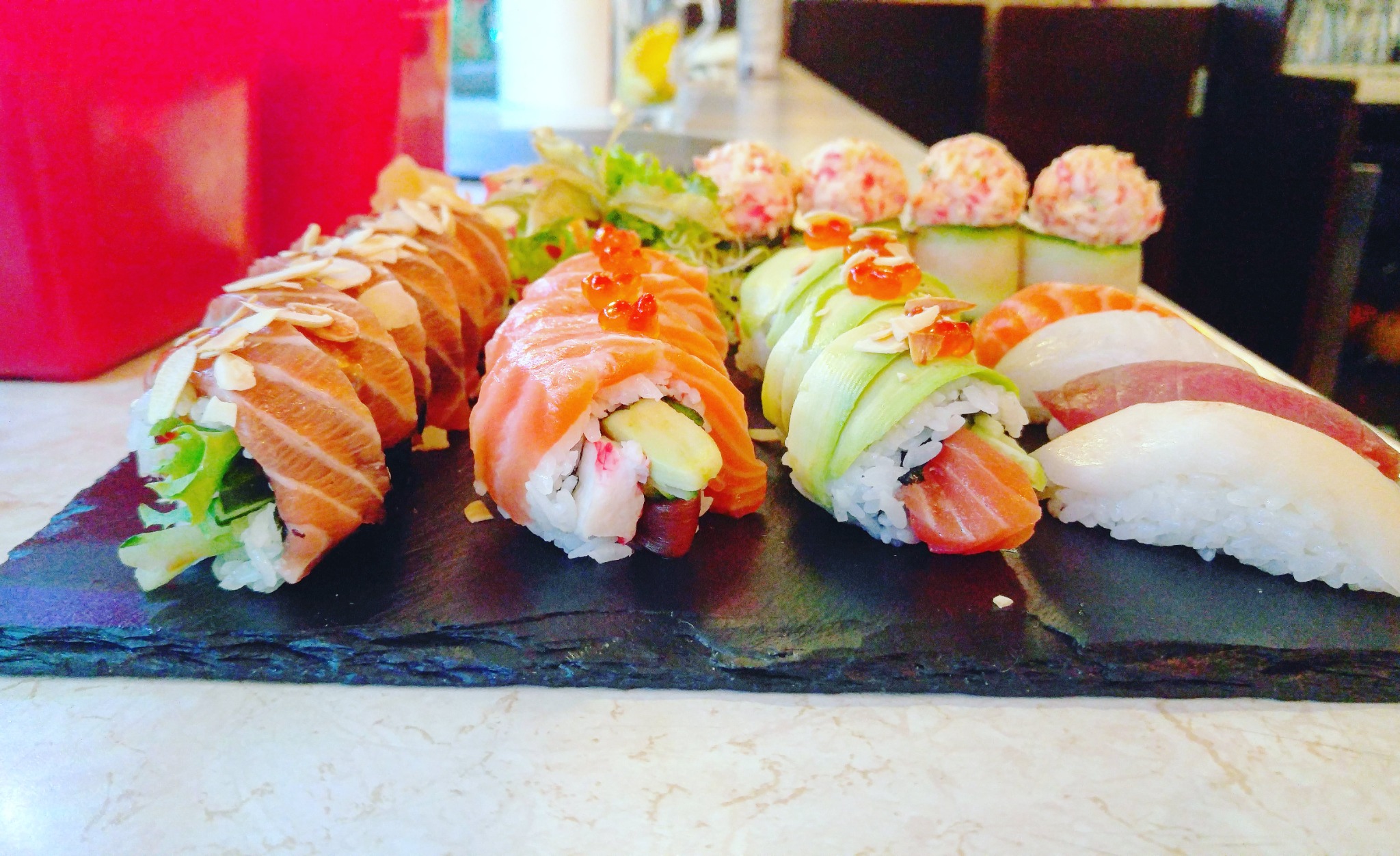 Zestaw sushi z łososiem, tuńczykiem i awokado, podany na czarnym kamieniu we Wrocławiu. Rolki ozdobione migdałami i kawiorem.