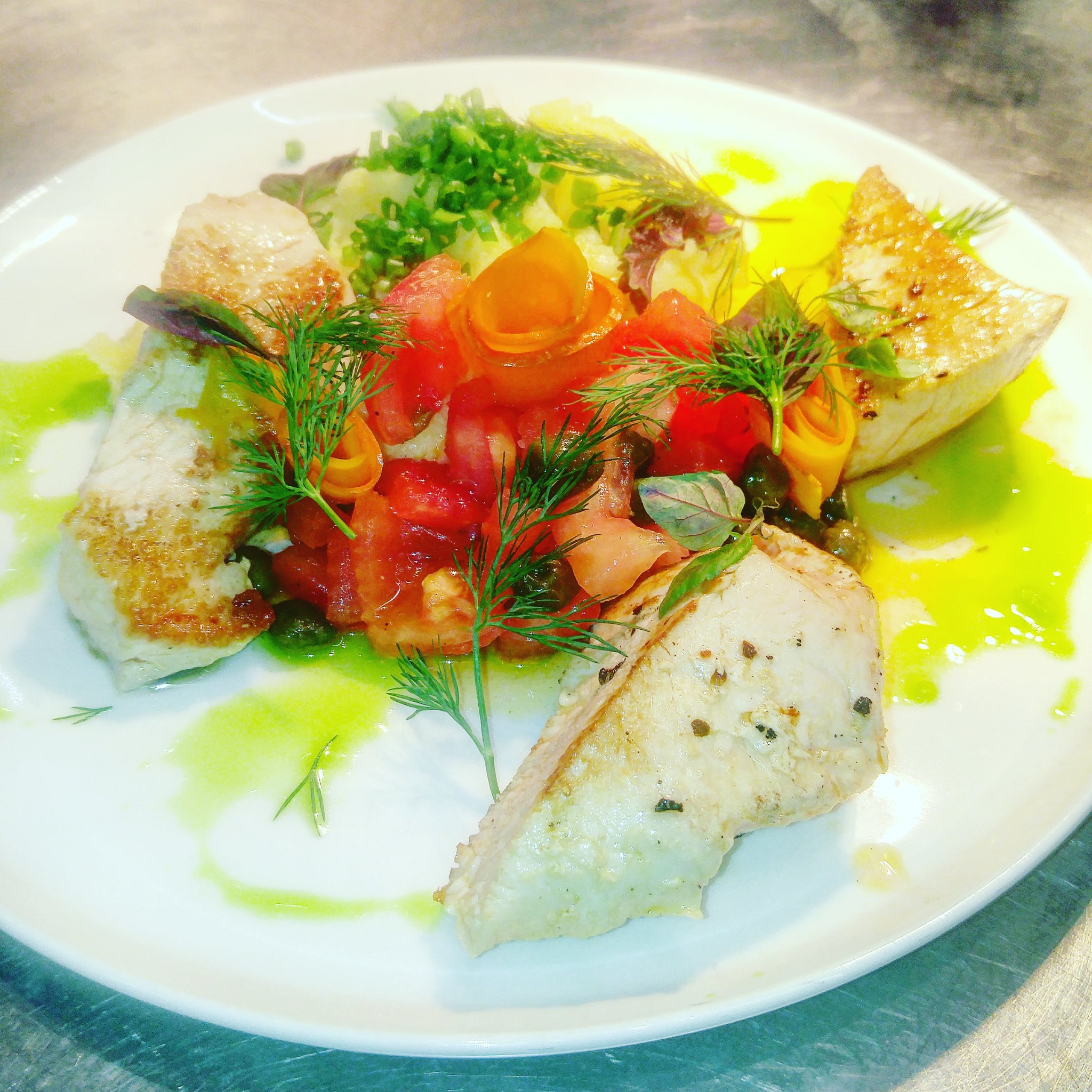 Elegancko podane danie z grillowanej ryby, pomidorów ułożonych w kształt róży, z dodatkiem świeżego koperku i sosem na białym talerzu.