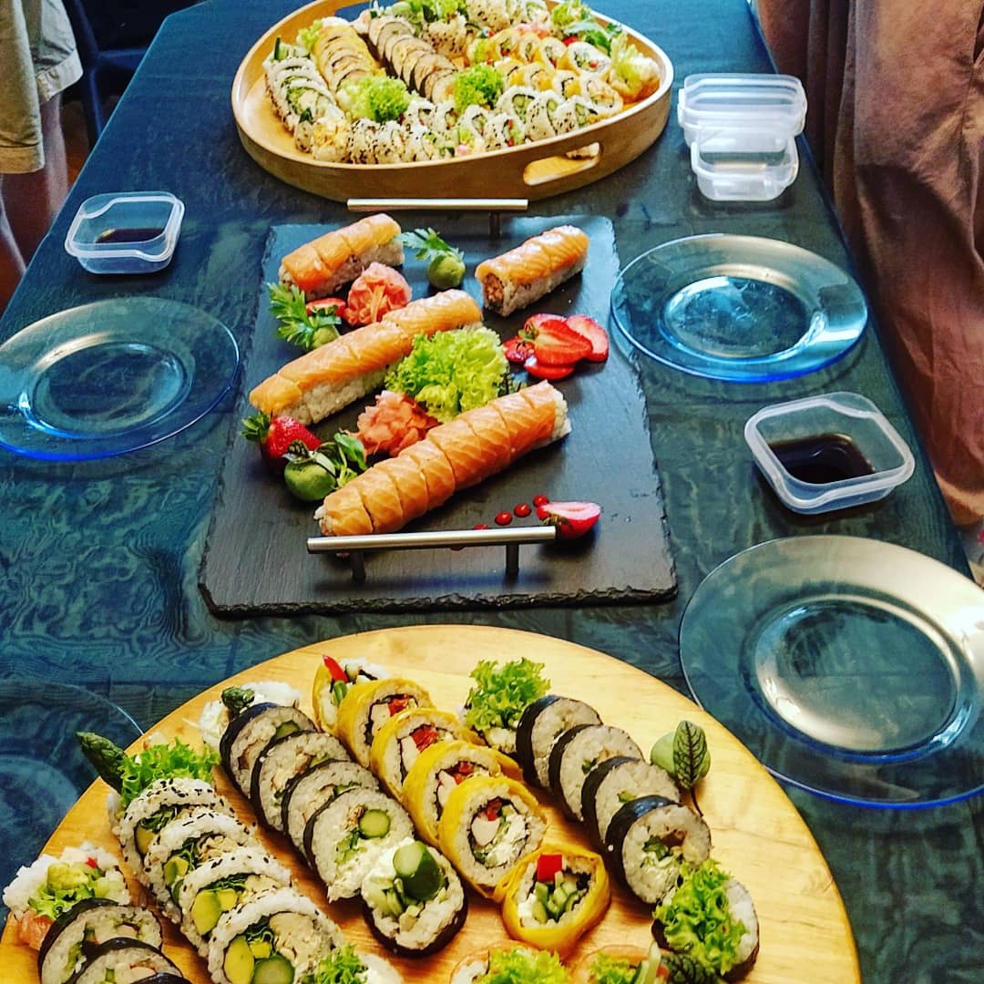 Zestaw sushi z różnymi rolkami, w tym z łososiem i warzywami, ułożony na drewnianych i łupkowych deskach, z dodatkami w postaci sosu sojowego, imbiru i truskawek, przygotowany do serwowania...