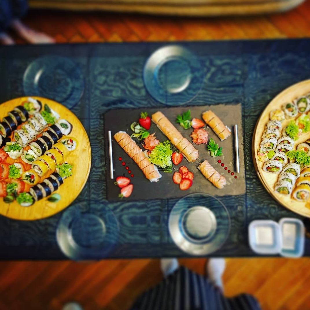 Zestaw sushi na drewnianych i łupkowych deskach, udekorowany truskawkami, imbirem i sałatą, widok z góry z elementami stroju osoby fotografującej.