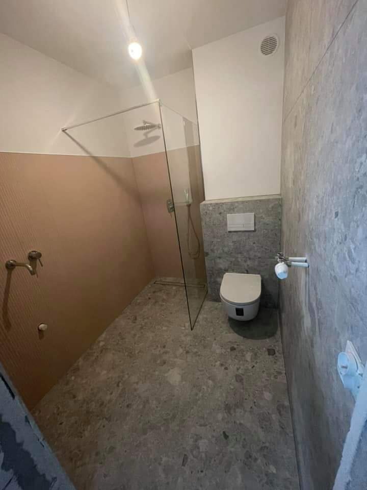 Nowoczesna łazienka z kabiną prysznicową bez brodzika, wykończona płytkami w odcieniach szarości i beżu, z widocznym odpływem liniowym w podłodze.