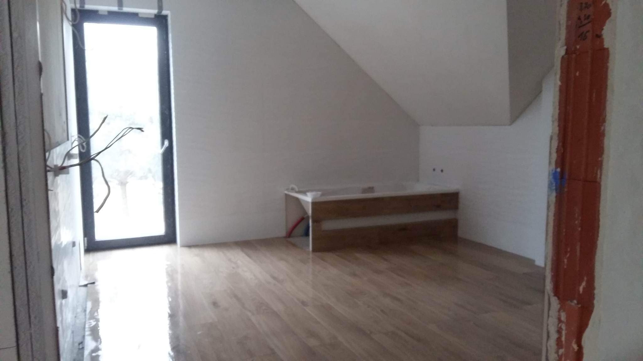 Wnętrze poddasza w trakcie remontu w Sochaczewie, widoczne surowe ściany, drewniana podłoga i przygotowane miejsce na wannę, instalacja elektryczna częściowo wyprowadzona.