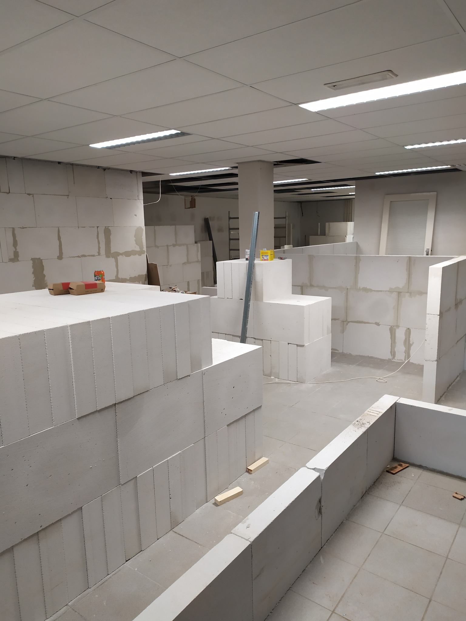 Wnętrze biurowe w trakcie przebudowy z wykorzystaniem białych bloczków betonowych, widoczne przygotowane ściany działowe i materiały budowlane.