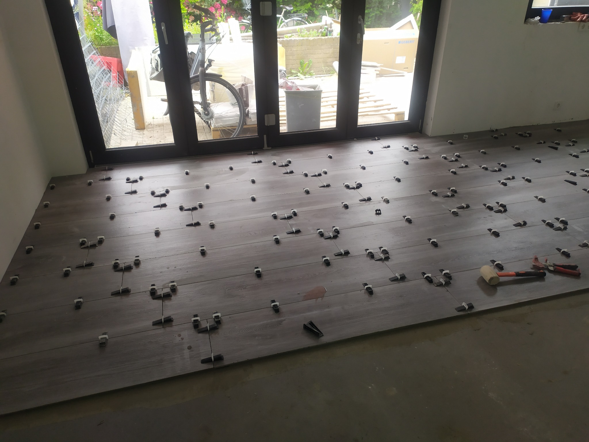 Układanie płytek podłogowych imitujących drewno z użyciem klipsów poziomujących, widoczny gumowy młotek i szczypce do klipsów