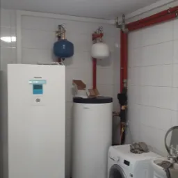 Kotłownia we Wrocławiu z nowoczesnym piecem, zasobnikiem ciepłej wody i instalacją hydrauliczną na tle białych płytek.