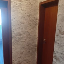 Dominik Hanek - Fragment wnętrza z dwiema parami drzwi, ściana wykończona imitacją starej cegły z widocznymi nierównościami.