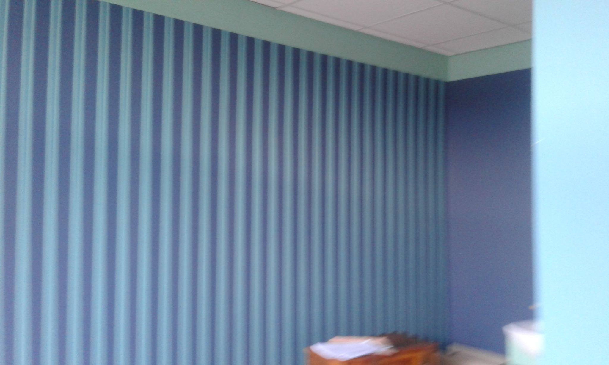 Ściana w pokoju w Szczurowej z nowo położoną tapetą w pionowe, niebiesko-błękitne pasy, z widoczną listwą sufitową w kolorze miętowym i fragmentem niebieskiej ściany obok.