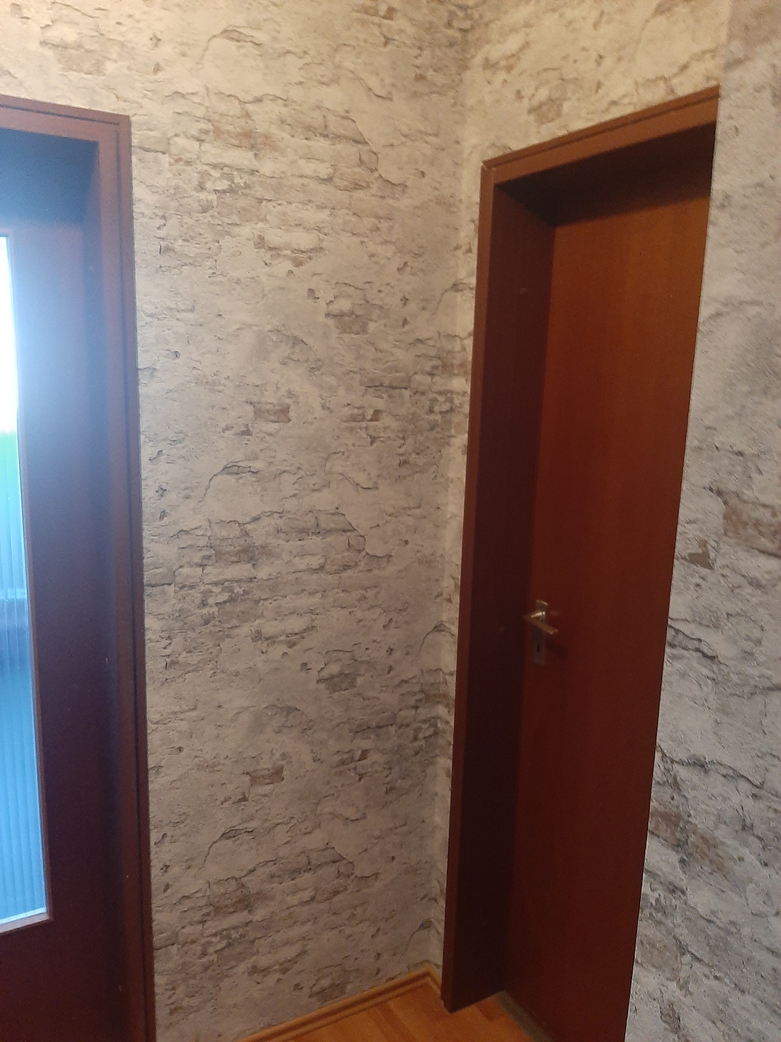 Fragment wnętrza z dwiema parami drzwi, ściana wykończona imitacją starej cegły z widocznymi nierównościami.