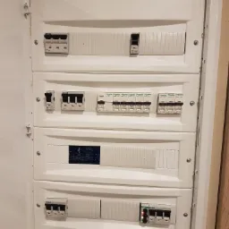 Otwarta, biała skrzynka rozdzielcza z różnymi wyłącznikami firm Eaton i Schneider Electric, widoczny wyświetlacz z parametrami, zamontowana na ścianie.