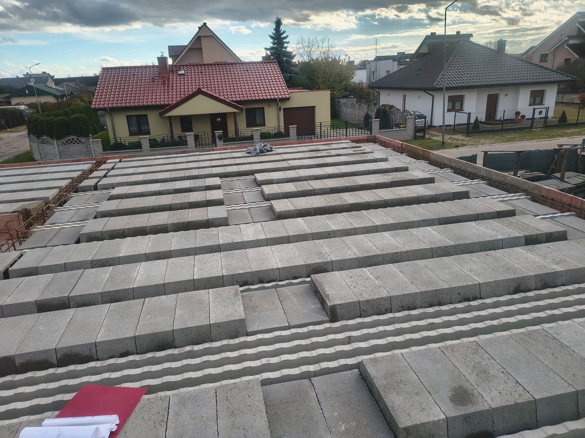 Wieniec stropowy z szalunkiem traconym i ułożonymi bloczkami betonowymi na budowie domu jednorodzinnego. Widoczne zbrojenie i plany budowlane.