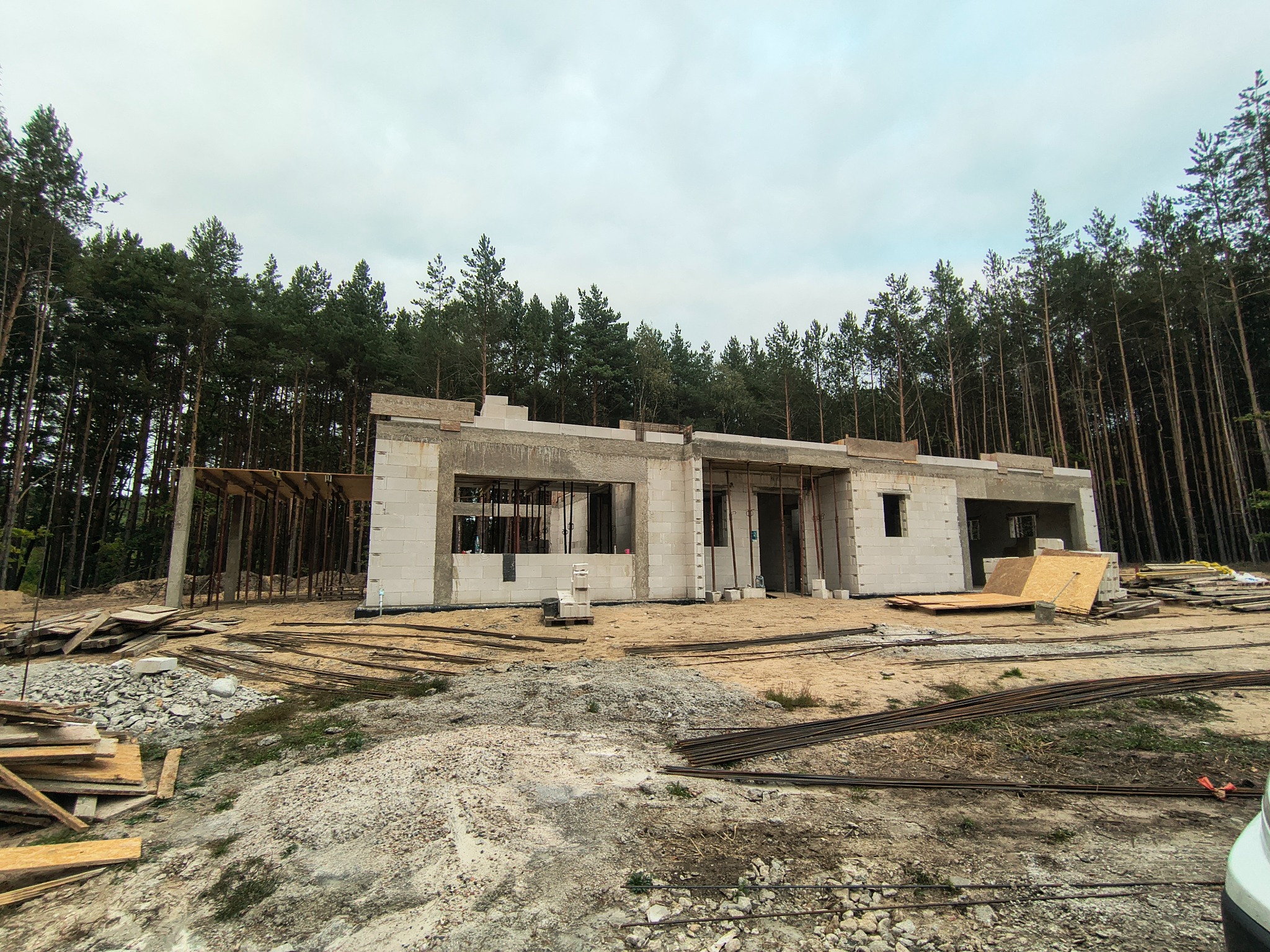 Surowy stan domu z betonu komórkowego w lesie, widok z zewnątrz. Widoczne szalunki i materiały budowlane. Etap budowy przed elewacją i wykończeniem.
