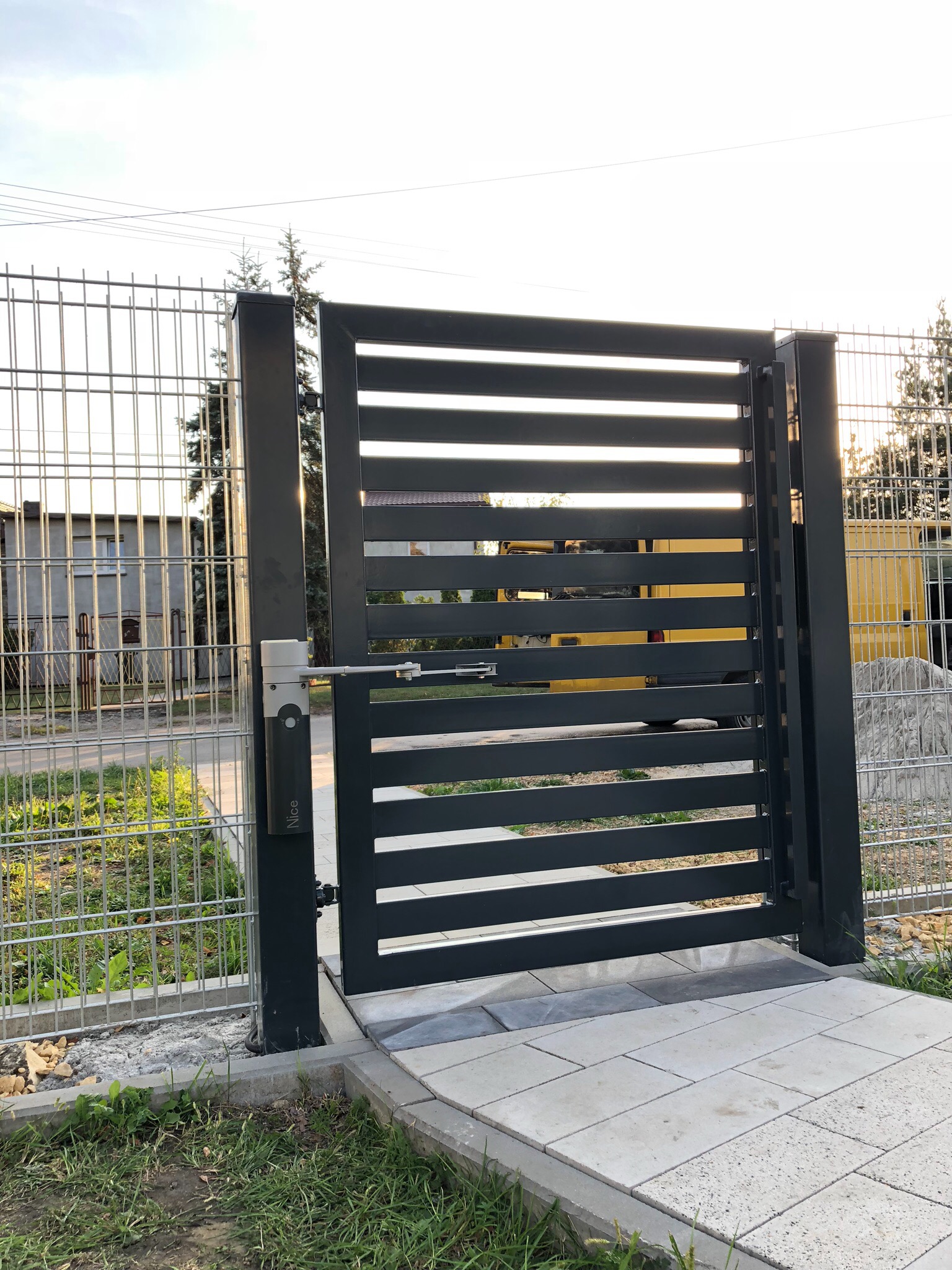 Nowoczesna, przesuwna brama w kolorze antracytu z automatyką firmy Nice, zamontowana przy posesji z ogrodzeniem panelowym.
