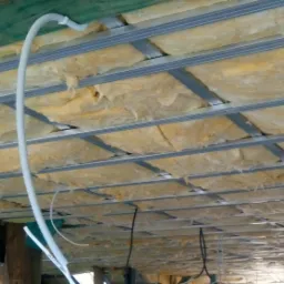 Poddasze w trakcie ocieplania wełną mineralną, widoczne metalowe profile konstrukcyjne i biała rura instalacyjna.