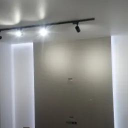 Wnętrze po remoncie z szarą ścianą, oświetleniem szynowym z reflektorami i wnękami oświetleniowymi po bokach ściany.