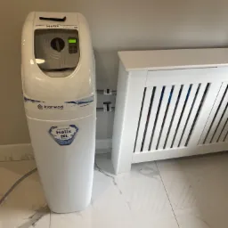 Biały zmiękczacz wody Klarwod Helix 20L, zainstalowany obok białego grzejnika z osłoną, na marmurowej podłodze.