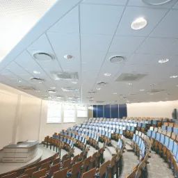 Sala wykładowa z rzędami krzeseł, oświetleniem sufitowym i systemem wentylacji z okrągłymi nawiewnikami