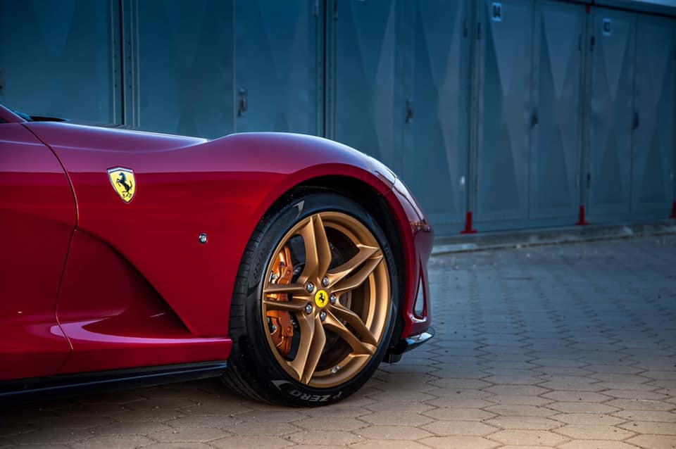 Czerwone Ferrari 812 Superfast z złotymi felgami na tle szarych garaży.