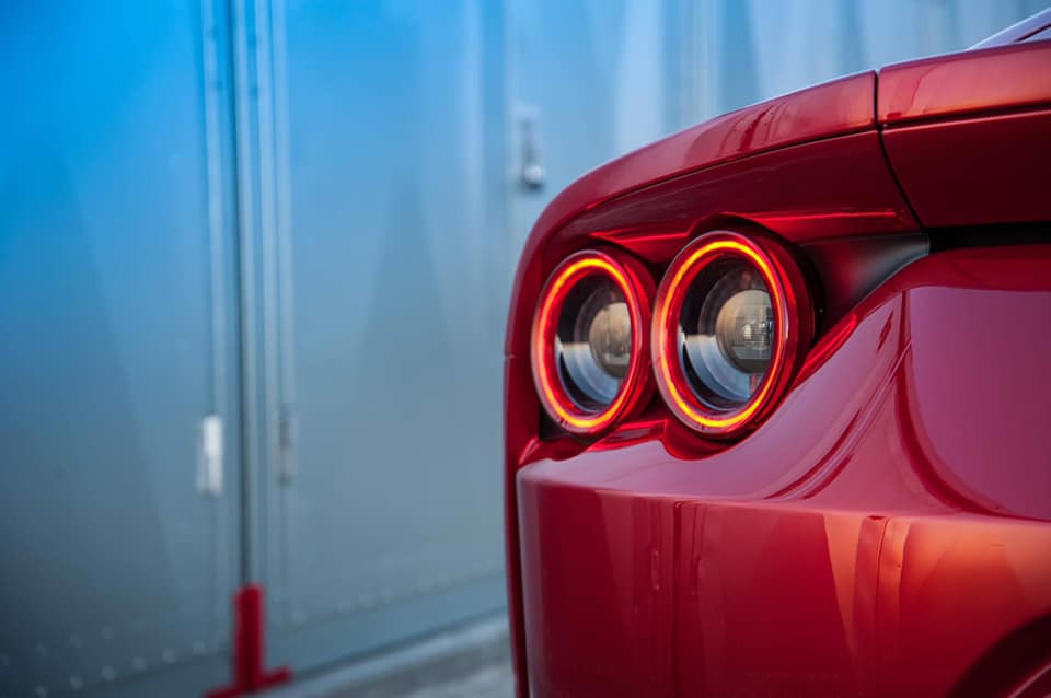 Czerwony samochód sportowy z okrągłymi światłami tylnymi, widok z tyłu na tle metalowej ściany garażu.