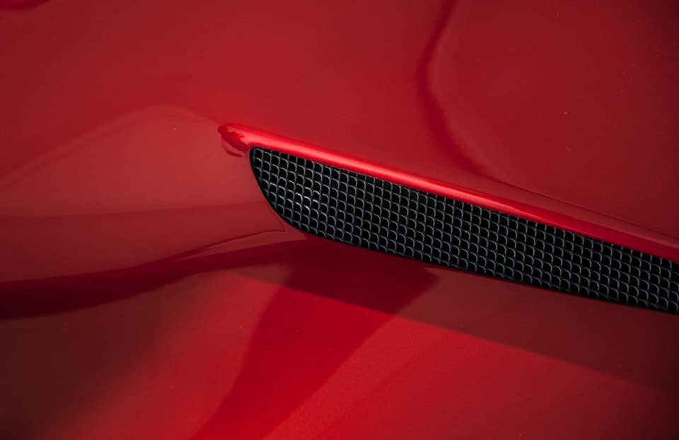 Czerwony lakier karoserii samochodu z czarną kratką wlotu powietrza i odbiciem światła.