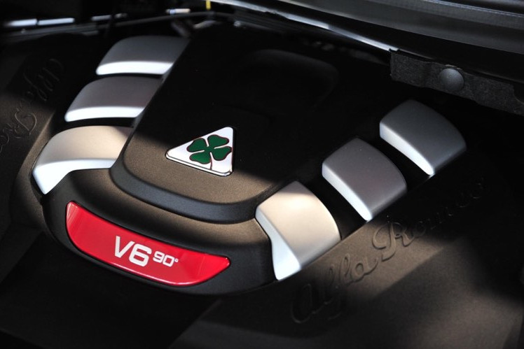 Silnik V6 90° Alfa Romeo z charakterystycznym logo czterolistnej koniczyny na czarnej obudowie z srebrnymi akcentami.