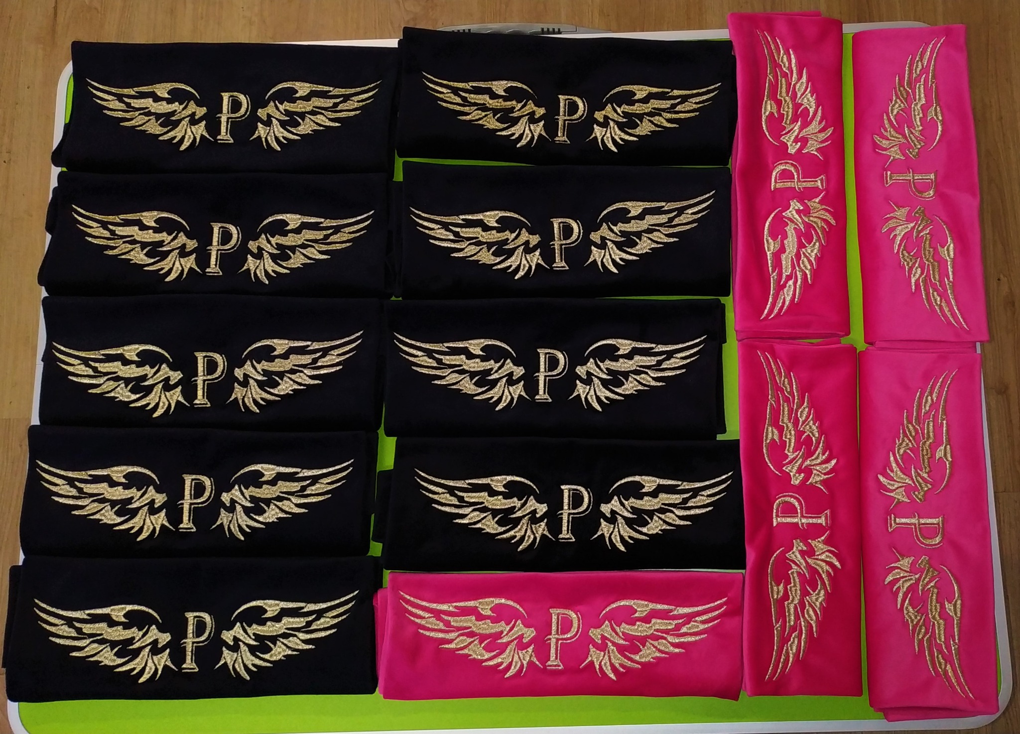 Czarno-różowe złożone koszulki z wyhaftowanym złotym motywem skrzydeł i literą 'P'.