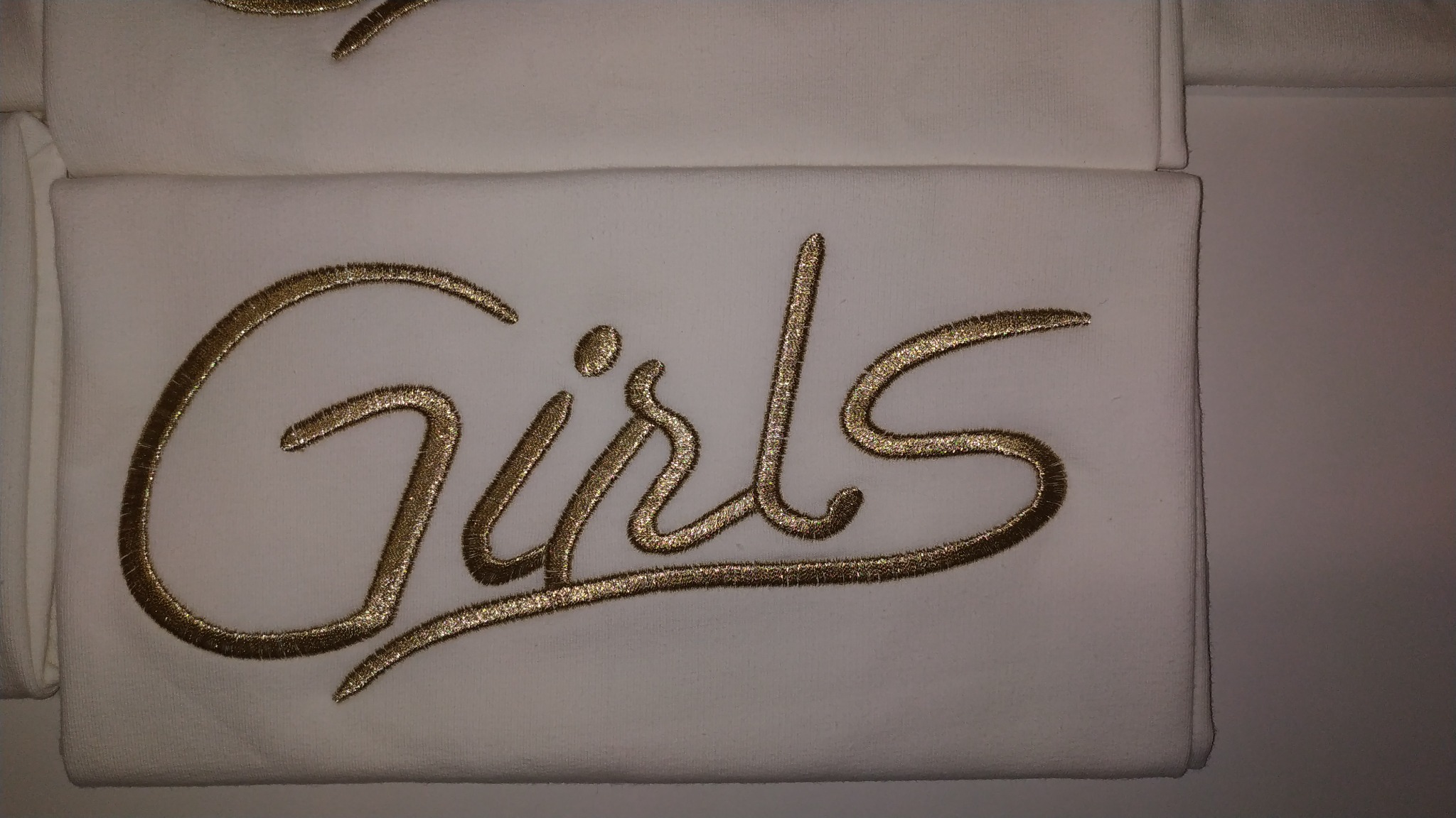 Biały ręcznik z wyhaftowanym złotą nicią napisem 'Girls'.