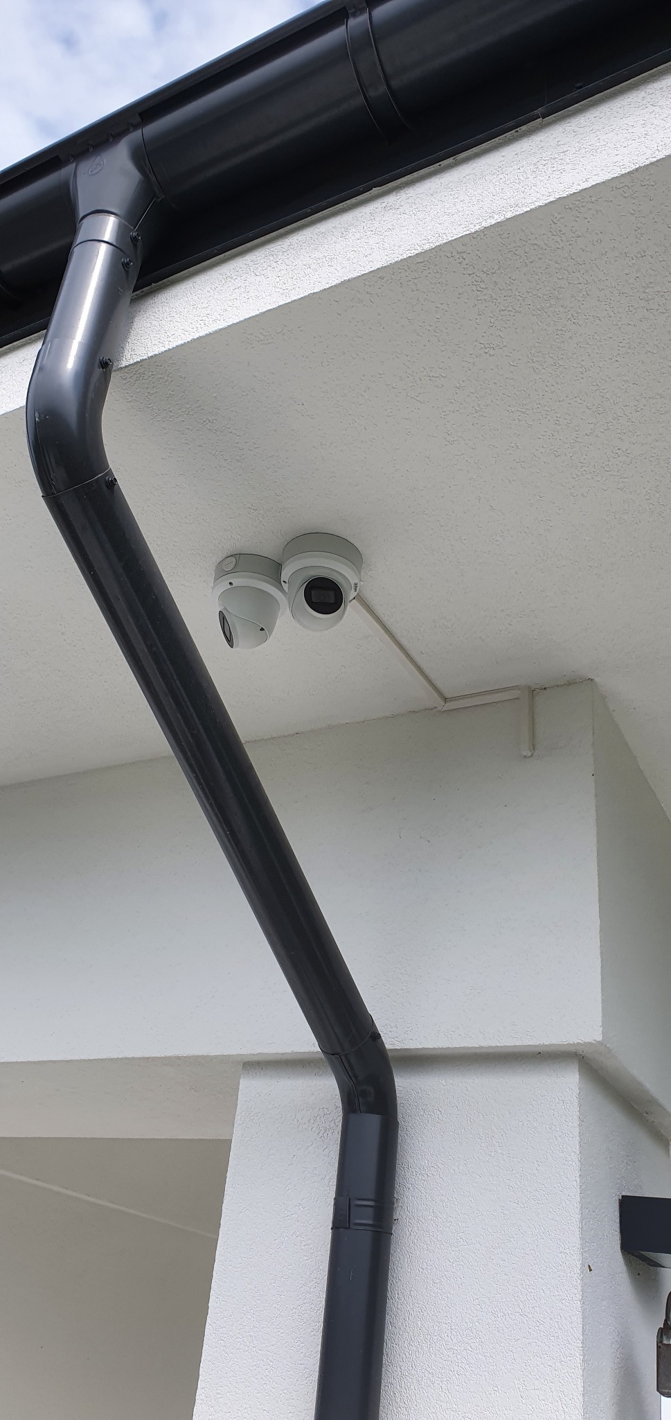 Dwie białe kamery monitoringu kopułkowe zamontowane pod okapem budynku z czarną rynną.