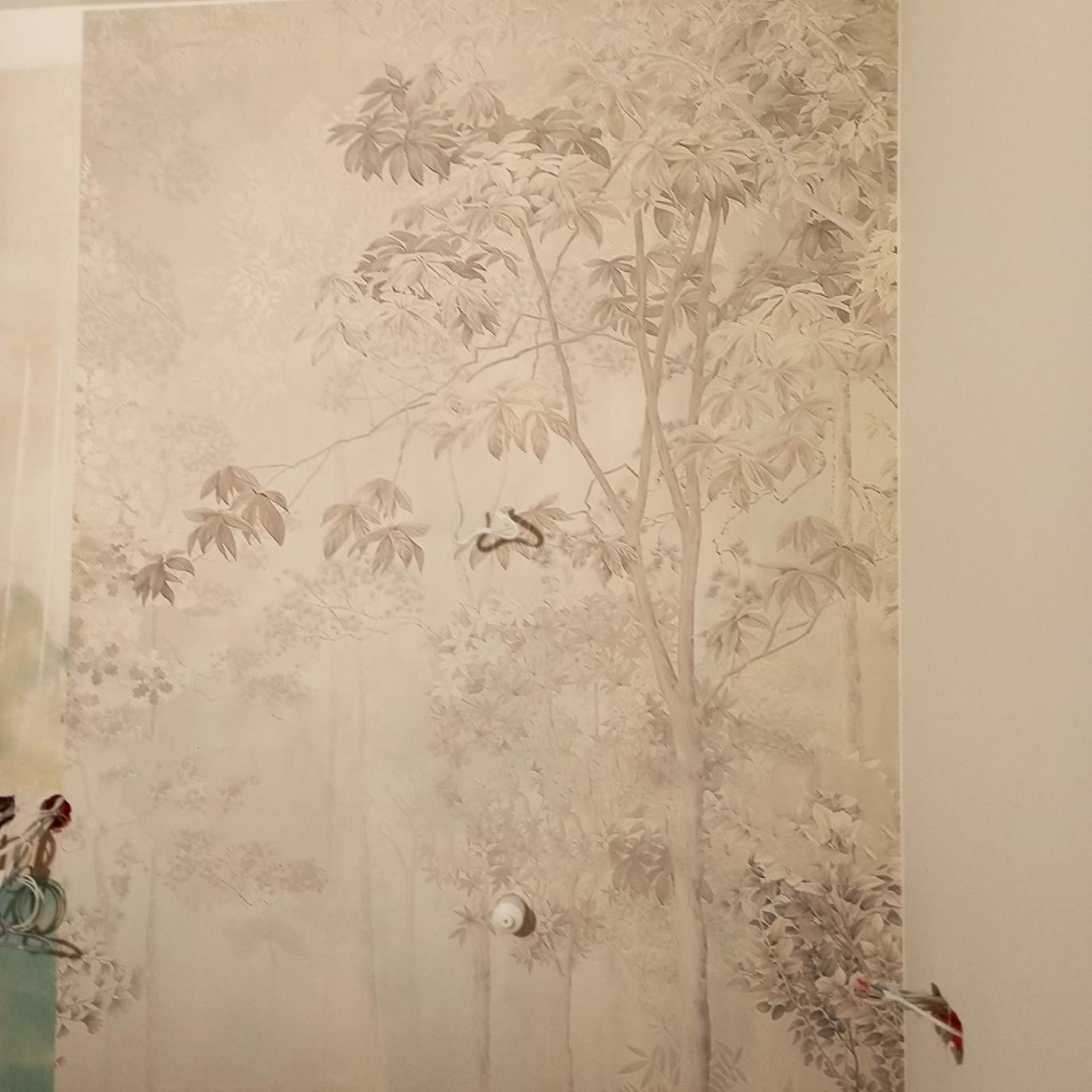 Ściana z beżową tapetą przedstawiającą drzewa w stylu vintage, z widocznym włącznikiem światła i fragmentem rośliny w doniczce w lewym dolnym rogu.