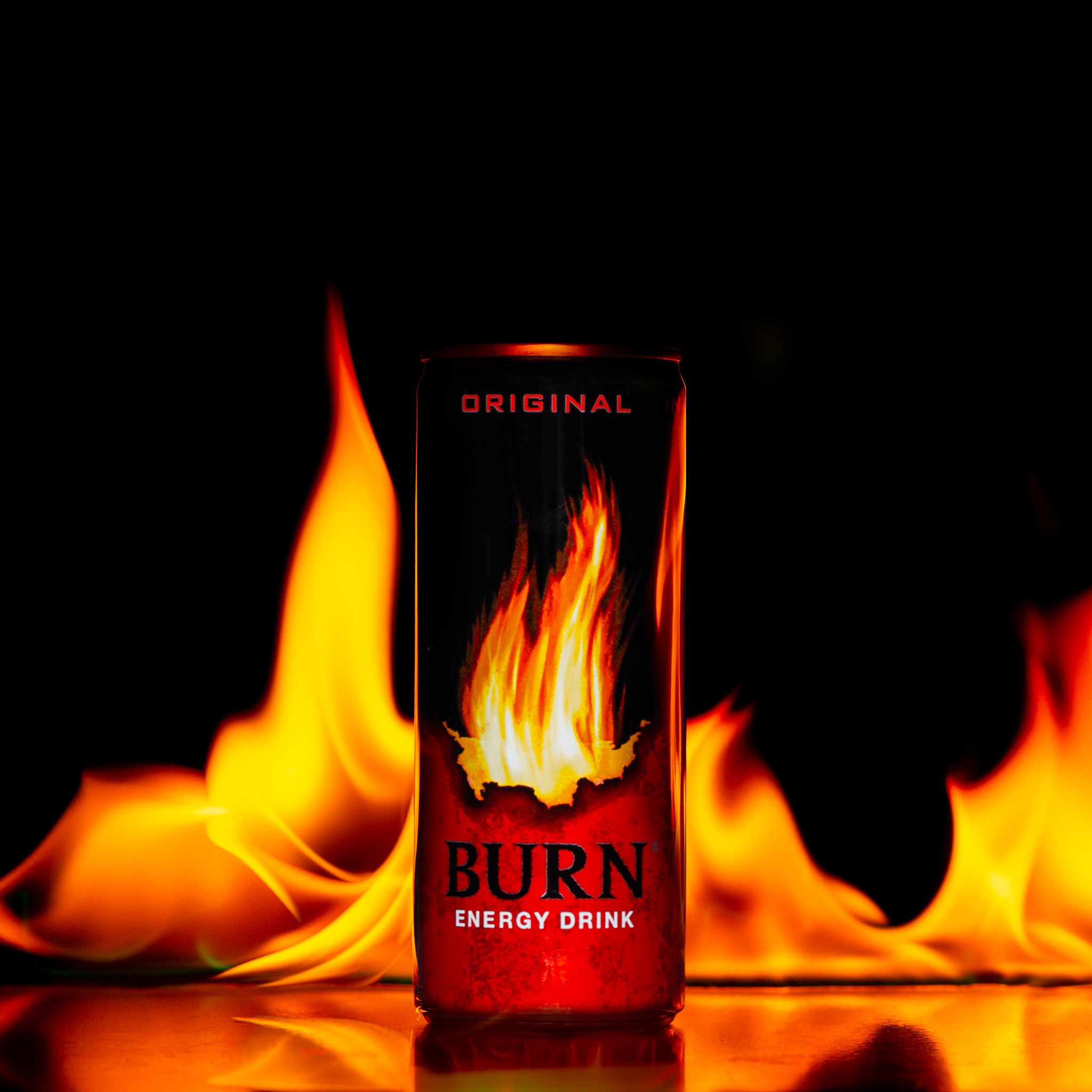Puszka napoju energetycznego Burn na tle płomieni ognia, z efektem lustrzanego odbicia na powierzchni.