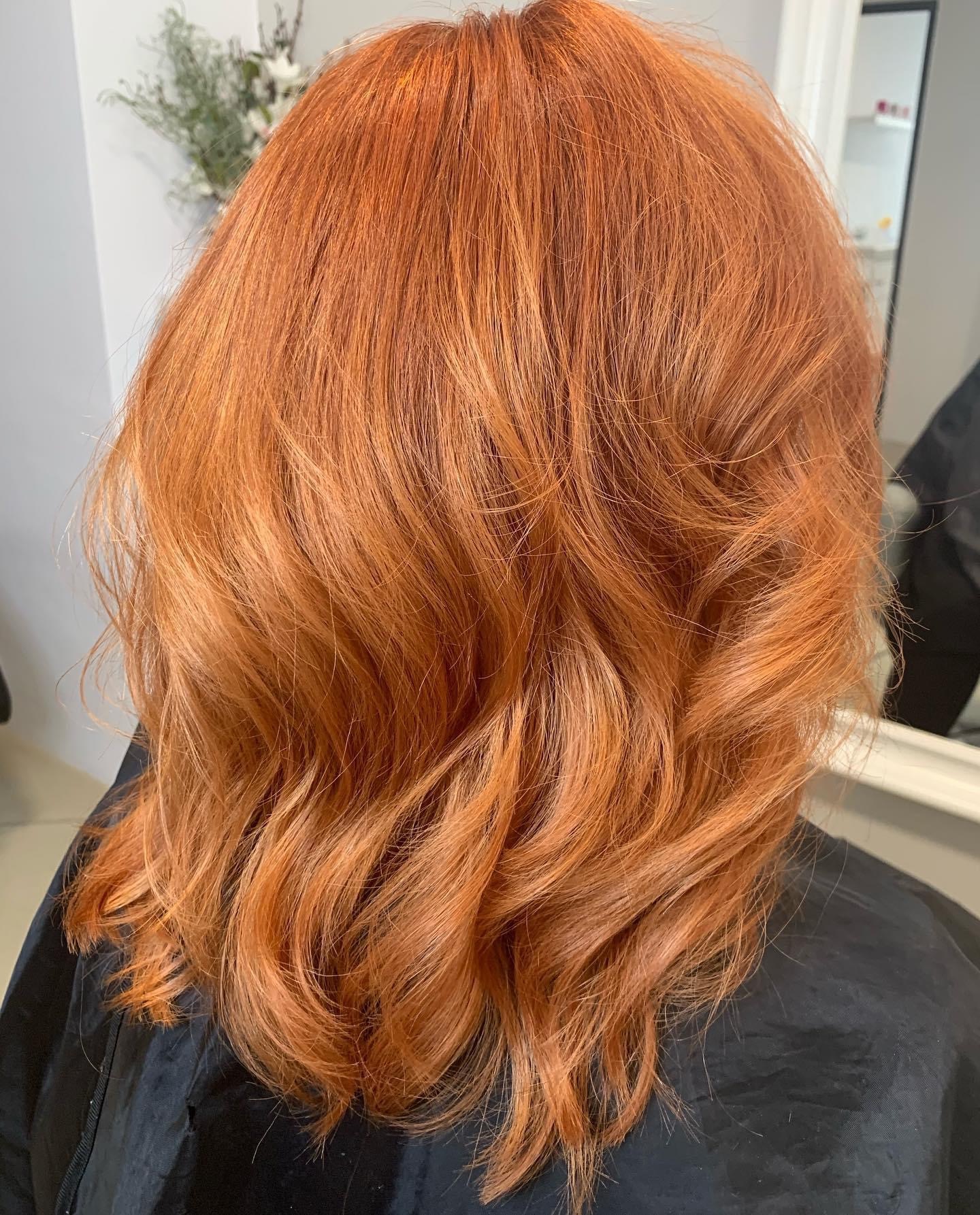 Miedziane włosy, delikatne fale, widok z tyłu, czarny ochraniacz na ramionach, refleks w lustrze w tle.