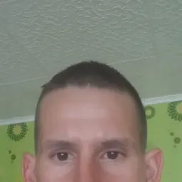 Portret mężczyzny z bliska na tle zielonej ściany w kwiaty i białego sufitu o wzorzystej strukturze.