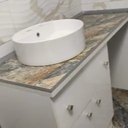 Biała, owalna umywalka nablatowa na szafce z czterema szufladami i blatem imitującym marmur, z płytkami ściennymi w tle o falistym wzorze.