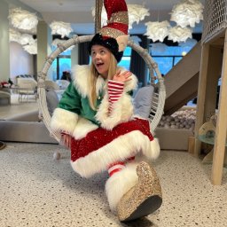 Wytwórnia Przyjęć - Uśmiechnięta animatorka w kostiumie elfa, siedząca na huśtawce w jasnym wnętrzu z dekoracyjnymi lampami. Widoczny fragment sali zabaw z kulkami.