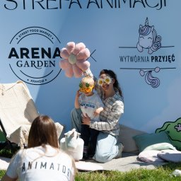 Wytwórnia Przyjęć - Strefa animacji: kobieta z dzieckiem w zabawnych okularach na tle dekoracji z jednorożcem. Animator w tle. Arena Garden Kraków.