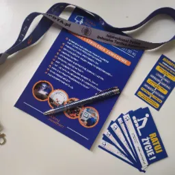 Ulotka informacyjna z ofertą szkoleń zawodowych, długopis, smycz z logo firmy szkoleniowej, wizytówki i schemat postępowania przy resuscytacji krążeniowo-oddechowej, ułożone na białym tle.