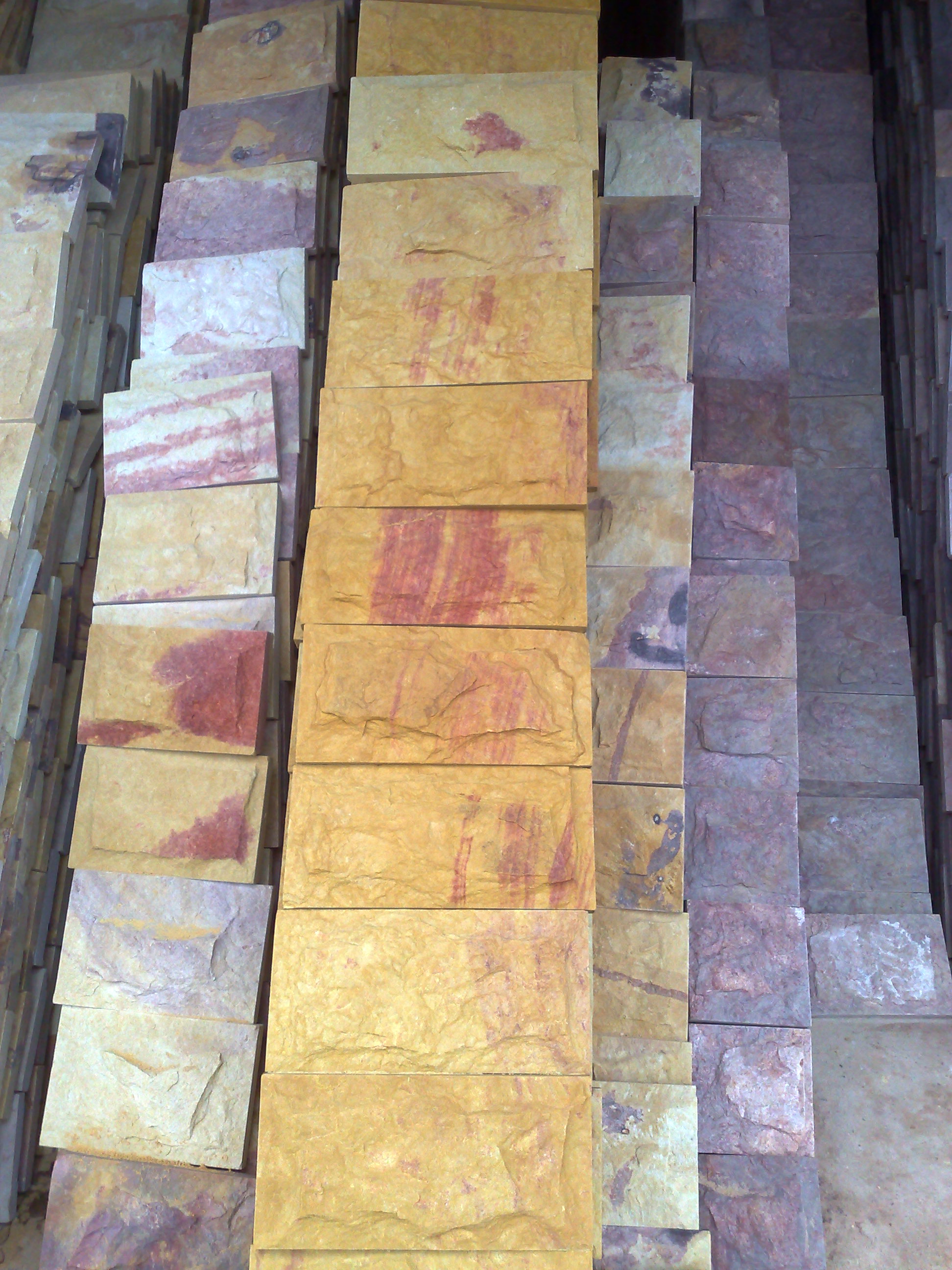 Stosy płytek kamiennych w odcieniach beżu, brązu i szarości, ułożone w rzędach, wykazujące naturalne wzory i tekstury kamienia.