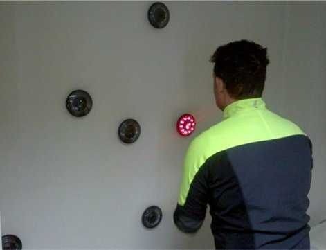 Mężczyzna w neonowo-żółtej kurtce instaluje okrągłe, podświetlane na czerwono panele LED na białej ścianie.