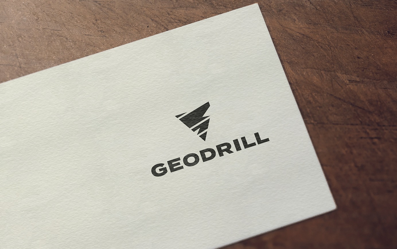 Logo firmy Geodrill w kolorze czarnym, umieszczone na białej wizytówce leżącej na drewnianym tle.