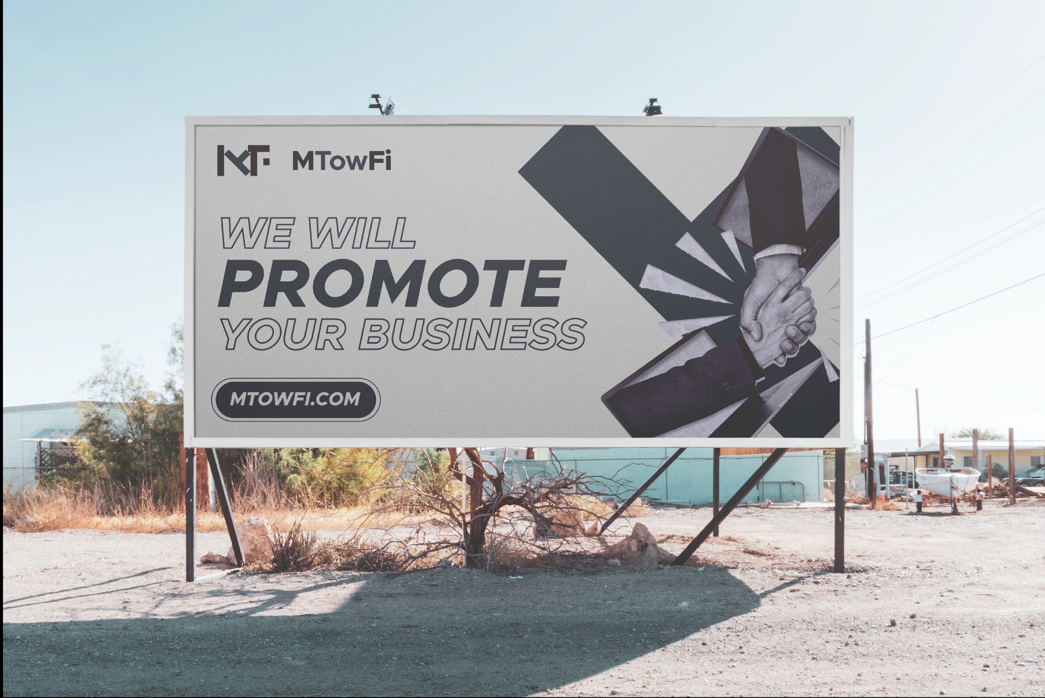 Billboard reklamowy MTowFi z grafiką dłoni w uścisku, umieszczony na pustkowiu z suchą roślinnością.