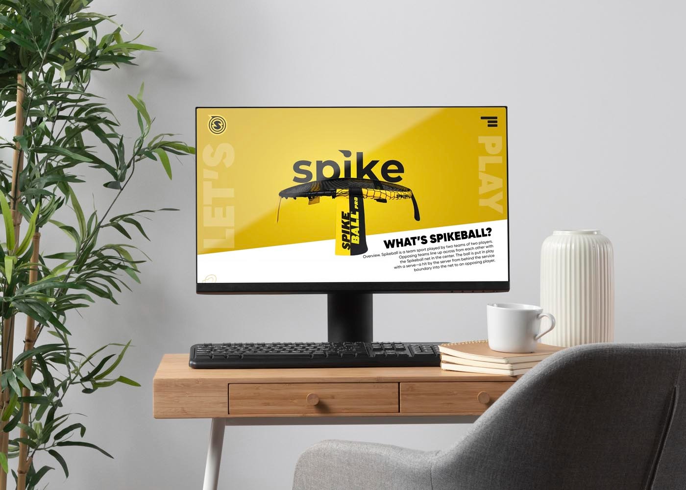 Ekran monitora wyświetla grafikę z logo i informacjami o Spikeballu, ustawiony na drewnianym biurku z minimalistycznymi dekoracjami: roślina doniczkowa, biały kubek i notatnik.