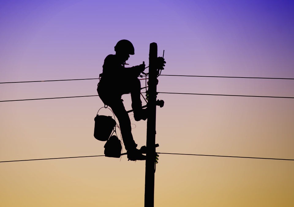 Sylwetka elektryka w kasku pracującego na słupie energetycznym na tle gradientu nieba o zmierzchu, z widocznymi przewodami i narzędziami.