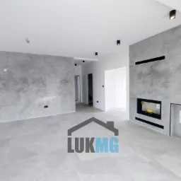 Nowoczesne wnętrze z szarymi ścianami wykończonymi dekoracyjną strukturą przypominającą beton, z wbudowanym kominkiem i dyskretnym oświetleniem punktowym.