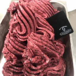 Porcja lodów jagodowych w metalowej kuwecie, z czarną etykietą producenta 'Wytwórnia Lodów z Kórnika'.