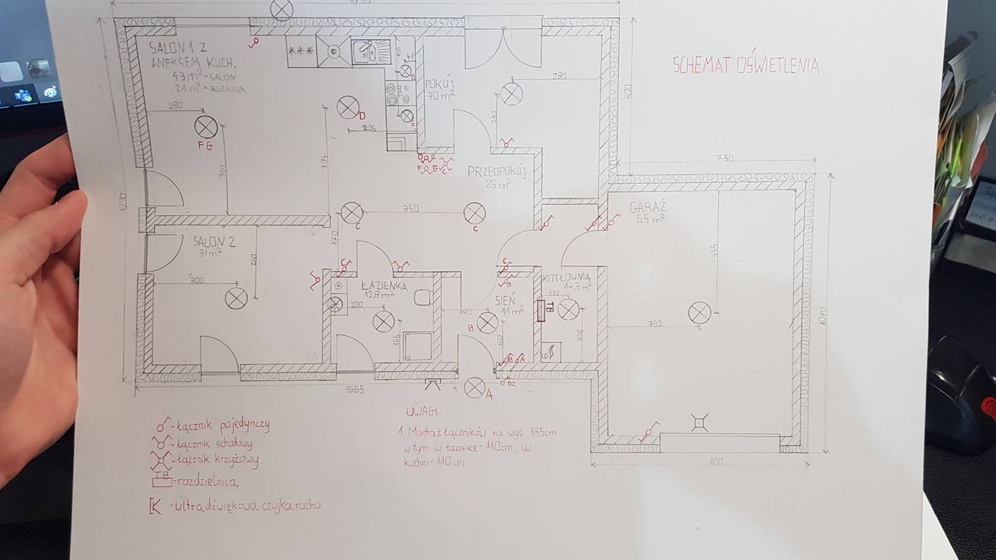 Ręcznie rysowany schemat oświetlenia mieszkania z zaznaczonymi punktami świetlnymi, przełącznikami i uwagami dotyczącymi wysokości montażu, trzymany w dłoni.
