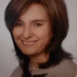 Portret uśmiechniętej kobiety z brązowymi włosami do ramion i zielonymi oczami, ubrana w szarą bluzkę z ciemniejszymi paskami na ramionach.