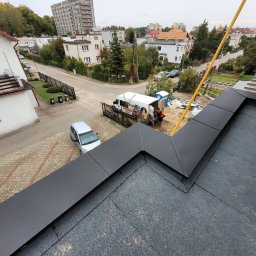 Dream Dach - Czarny, płaski dach z obróbkami blacharskimi, widok z góry na tle zabudowy miejskiej i ekipa dekarska przy samochodzie dostawczym z logo firmy.