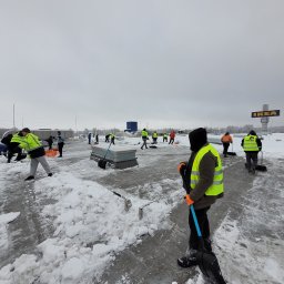 Dream Dach - Zespół pracowników w jaskrawych kamizelkach odblaskowych odśnieżających płaski dach dużego obiektu handlowego IKEA, z widocznymi łopatami i grubą warstwą śniegu.