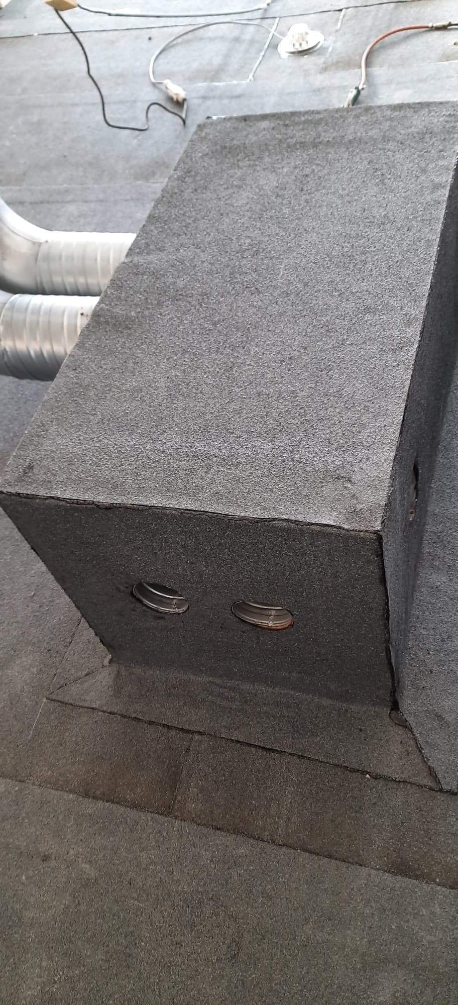 Szczegółowe ujęcie komina wentylacyjnego na dachu pokrytym papą, z widocznymi metalowymi wlotami powietrza i fragmentami instalacji elektrycznej w tle.