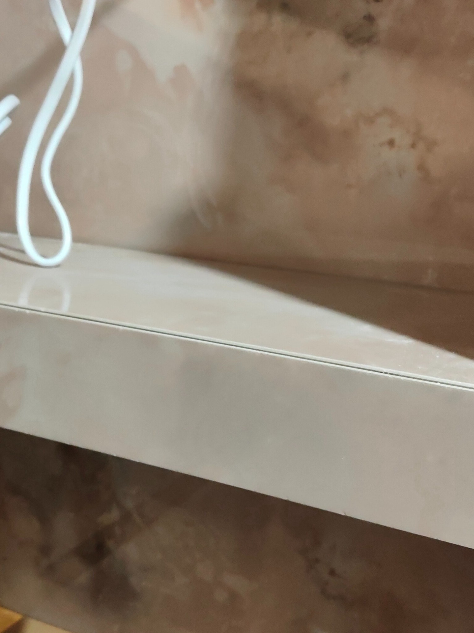 Półka z beżowego lakierowanego MDF na tle ściany z widocznymi zaciekami, ujęcie z dołu.